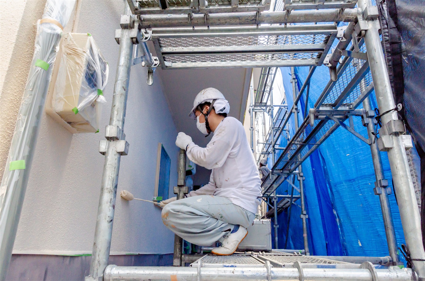 足場の上で住宅外壁を塗装する作業風景のイメージ